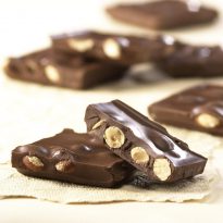 Milk Chocolate Almond Bark pieces on tan sheet. Large, thick pieces reveal chunks of almonds covered in milk chocolate.