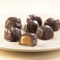 Vanilla Caramels are shown on a white plate. One (1) being open to reveal the vanilla caramel center. Rest are shown whole with dark chocolate drizzle.